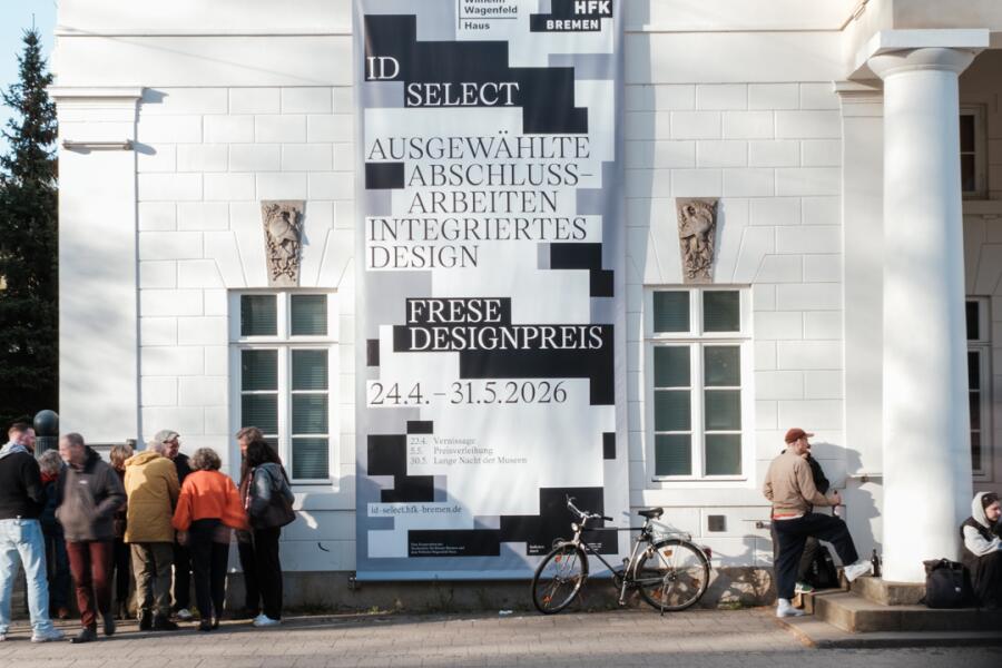 An der Außenwand hängt das großssformatige Banner mit Rechtecken und Schriftelementen in den Farben weiß, schwarz und grau