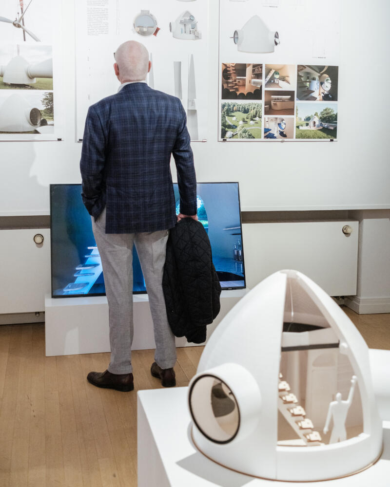 Ein Besucher schaut auf Plakate an der Wand. Vor ihm steht ein architektonisches Modell auf einem niedrigen Sockel.