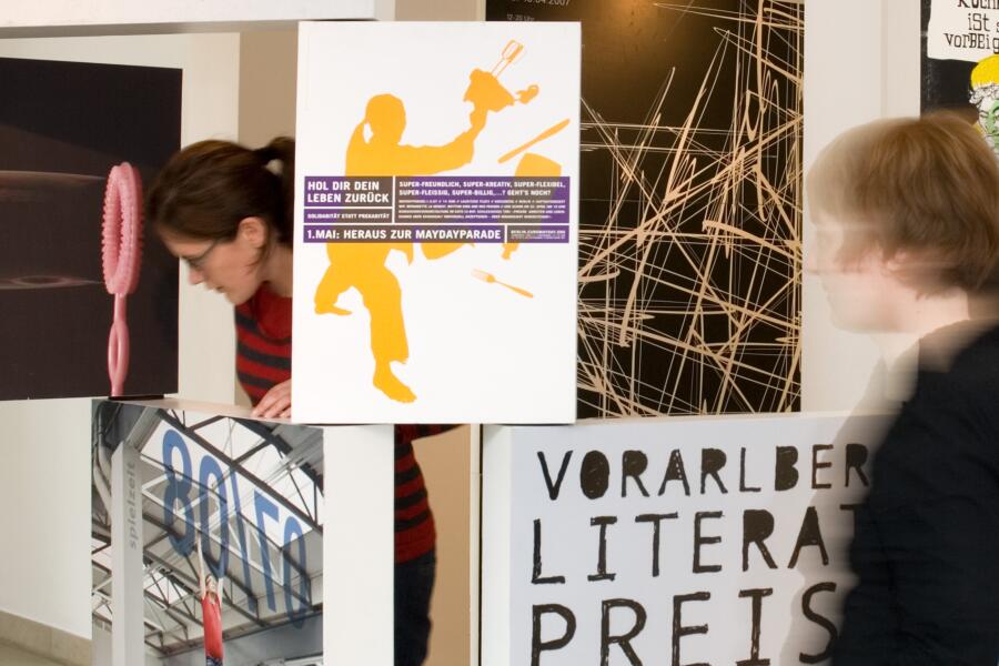 Bunte Plakate wurden auf schmalen, kastenförmigen Bildträgern aufgebracht und stehen nebeneinander und übereinander im Ausstellungraum.