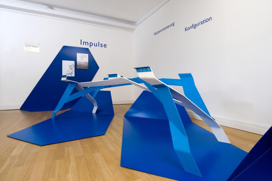 blaue Ausstellungsmodule wandern wie ein Band durch den Ausstellungsraum und bilden dabei Tischvitrinen.