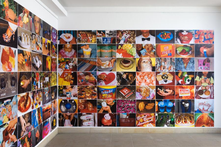 2 Wände im Ausstellungsraum sind vom Boden bis zur Decke mit knallbunten Fotos von Alltagsszenen bedeckt.
