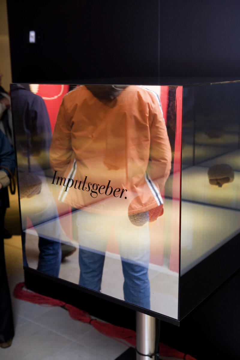 Auf der Scheibe einer Vitrine spiegeln sich Besucher der Ausstellung.